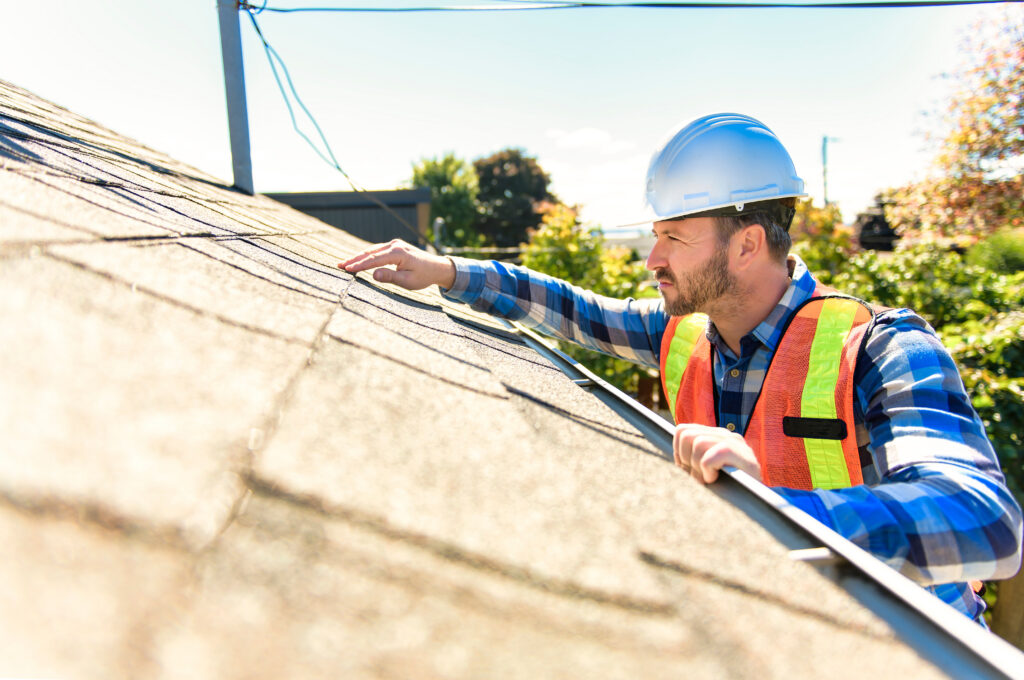 man with hard hat standing on steps inspecting house roof - roof repair - roofing inspection